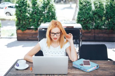 Sürpriz arıyor bir yaz kafede dizüstü kullanarak genç güzel kadın gözlük şok bir suratla. Tablo laptop, fincan kahve, dizüstü bilgisayar, telefon, kalem
