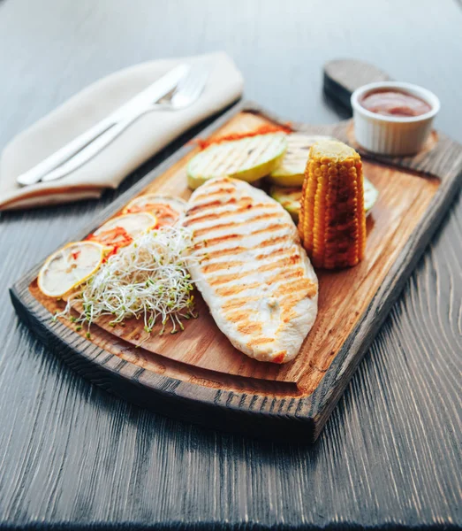 Grilled chicken fillet with vegetables and sauce on a wooden board