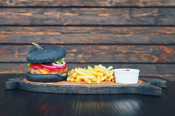 Hamburguesa negra con papas fritas y salsa en una tabla de madera — Foto de Stock