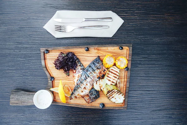 Pescado a la parrilla en una tabla de cortar de madera con verduras. fondo de madera. vista superior — Foto de Stock