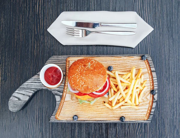 Fast food dish. Burger with fries on a wooden cutting board. Delicious hamburger and french fries with sauces. Cheeseburger with chicken meat