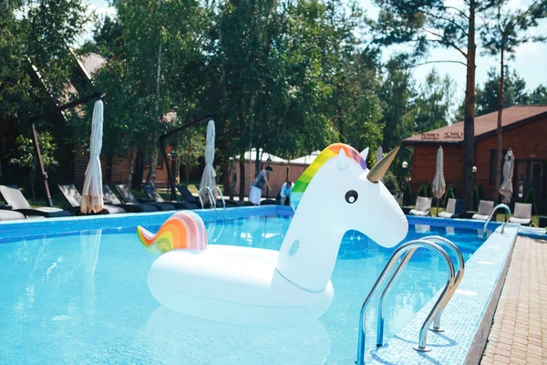 Unicornio inflable de color arco iris flotando en una piscina en el verano. Unicornio inflable blanco en la piscina — Foto de Stock