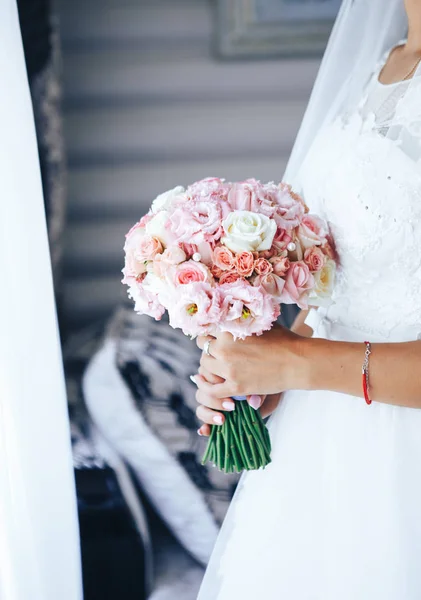 Noiva fica na janela e mantém um buquê de casamento. Close-up — Fotografia de Stock