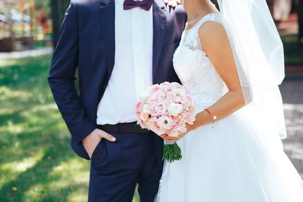 Noiva segura um buquê de casamento em mãos, o noivo abraça sua noiva juntos. Conceito de amante de casamento. Close-up — Fotografia de Stock