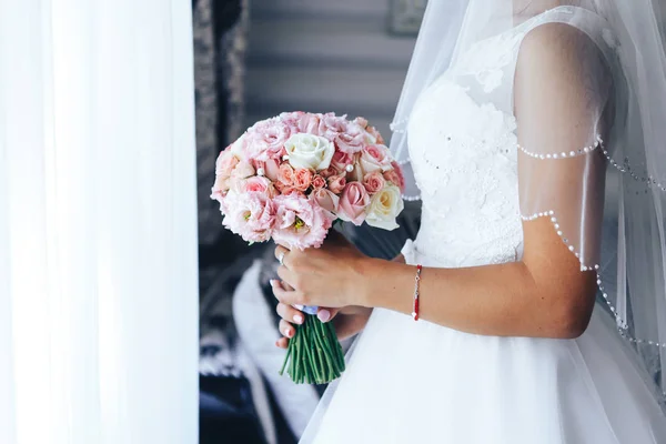 Noiva fica na janela e mantém um buquê de casamento. Close-up — Fotografia de Stock