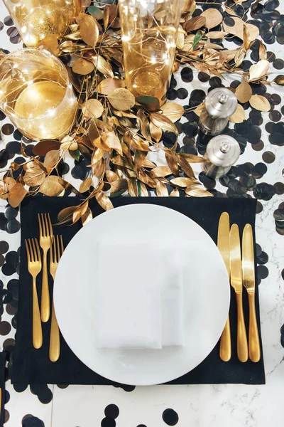 Il tavolo da pranzo è decorato in nero e oro. Ghirlanda in fiaschetta di vetro. Forchetta e coltello dorati — Foto Stock