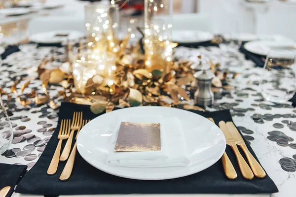 Tableis δείπνο διακόσμηση σε μαύρο και χρυσό. Γιρλάντα σε γυάλινη φιάλη. Χρυσό πιρούνι και μαχαίρι — Φωτογραφία Αρχείου