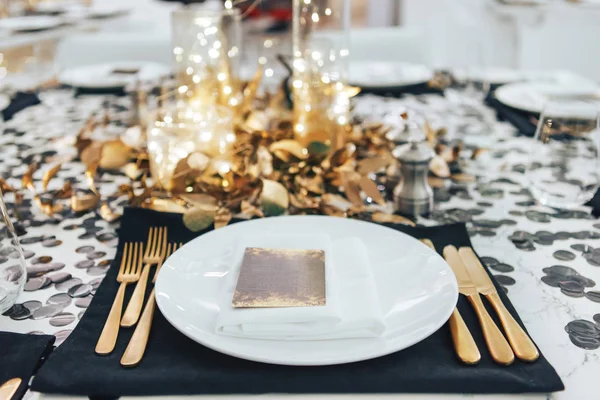 Večeře tableis laděné do černé a zlaté. Věnec ve skleněné baňce. Zlatá vidlička a nůž — Stock fotografie