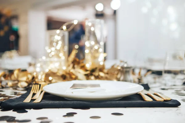 La mesa de la cena está decorada en negro y oro. Guirnalda en un frasco de vidrio. Tenedor y cuchillo dorado Imagen De Stock