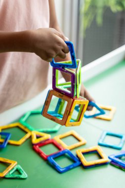 Manyetik geometrik şekil oyuncak ile oynayan pembe elbiseli kız, eller göstermek, hiçbir yüz.