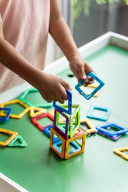 Manyetik geometrik şekil oyuncak ile oynayan pembe elbiseli kız, eller göstermek, hiçbir yüz.