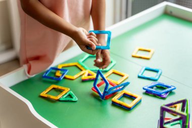 Manyetik geometrik şekil oyuncak ile oynayan pembe elbiseli kız, eller göstermek, hiçbir yüz.