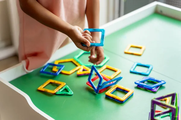Manyetik geometrik şekil oyuncak ile oynayan pembe elbiseli kız, eller göstermek, hiçbir yüz.