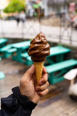 Elinde çikolatalı dondurma külahı tutan bir adam. Geçmişi çok bulanık, tarlanın derinliği çok az. Koyu arkaplan.