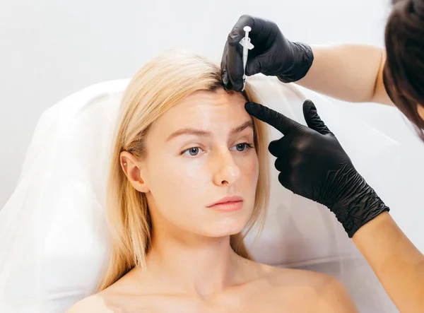 Portrait of attractive blonde model making injection in forehead. Perfection wellbeing wellness concept