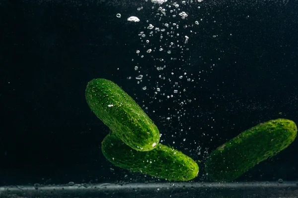 Green cucumbers in water on a black background.