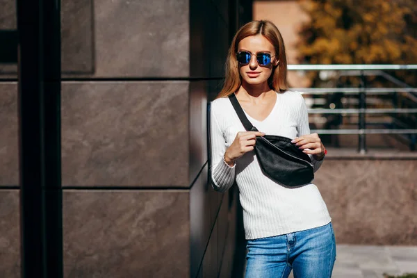 Stylish model girl at the city in glasses with waist bag