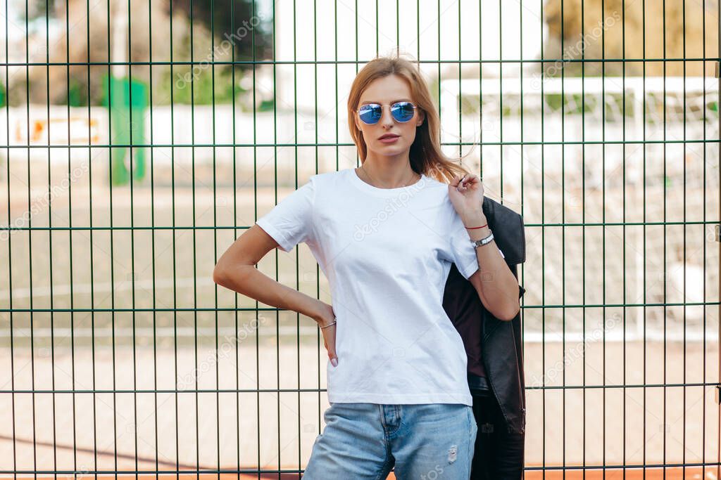 Blonde girl wearing t-shirt and  glasses posing against street , urban clothing style. Street photography