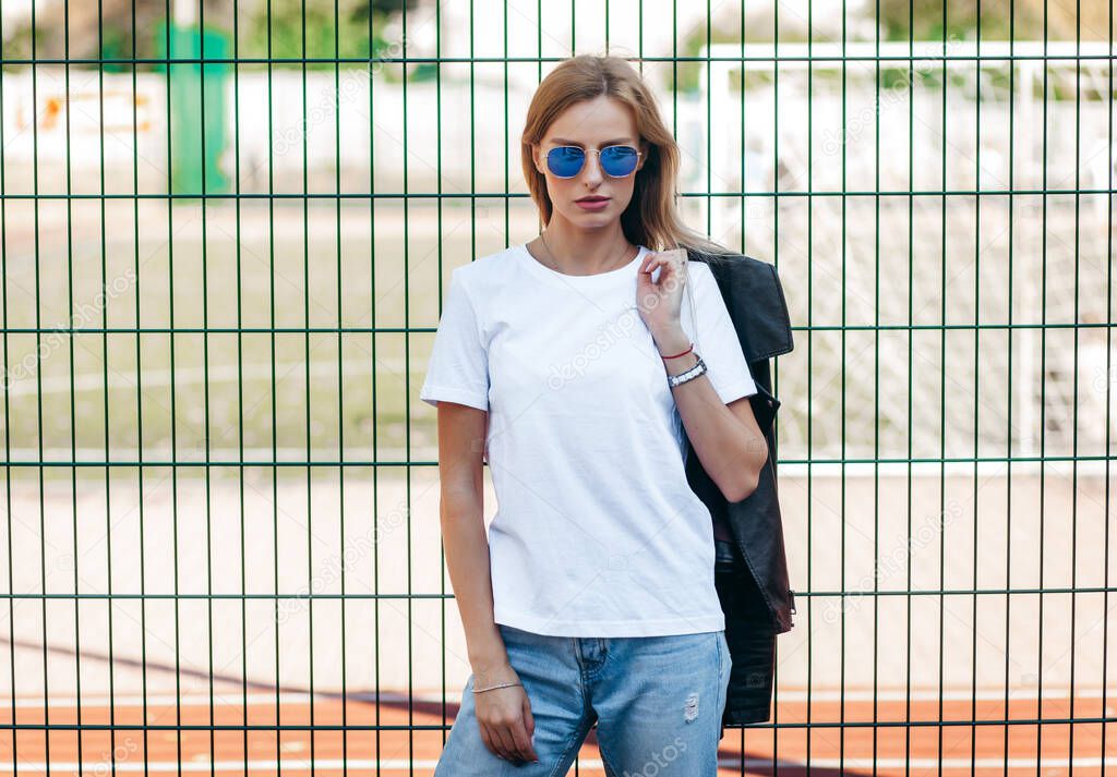 Blonde girl wearing t-shirt and  glasses posing against street , urban clothing style. Street photography