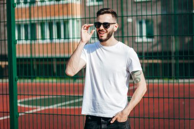 Beyaz tişörtlü ve gözlüklü, sakallı, şık bir genç. Sokak fotoğrafı