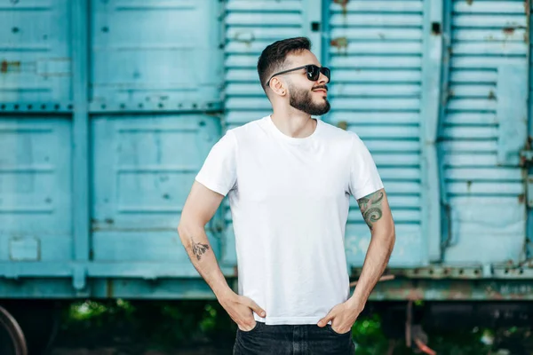 Young stylish man with a beard in a white T-shirt and glasses. Street photo