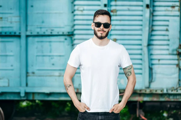 Young stylish man with a beard in a white T-shirt and glasses. Street photo
