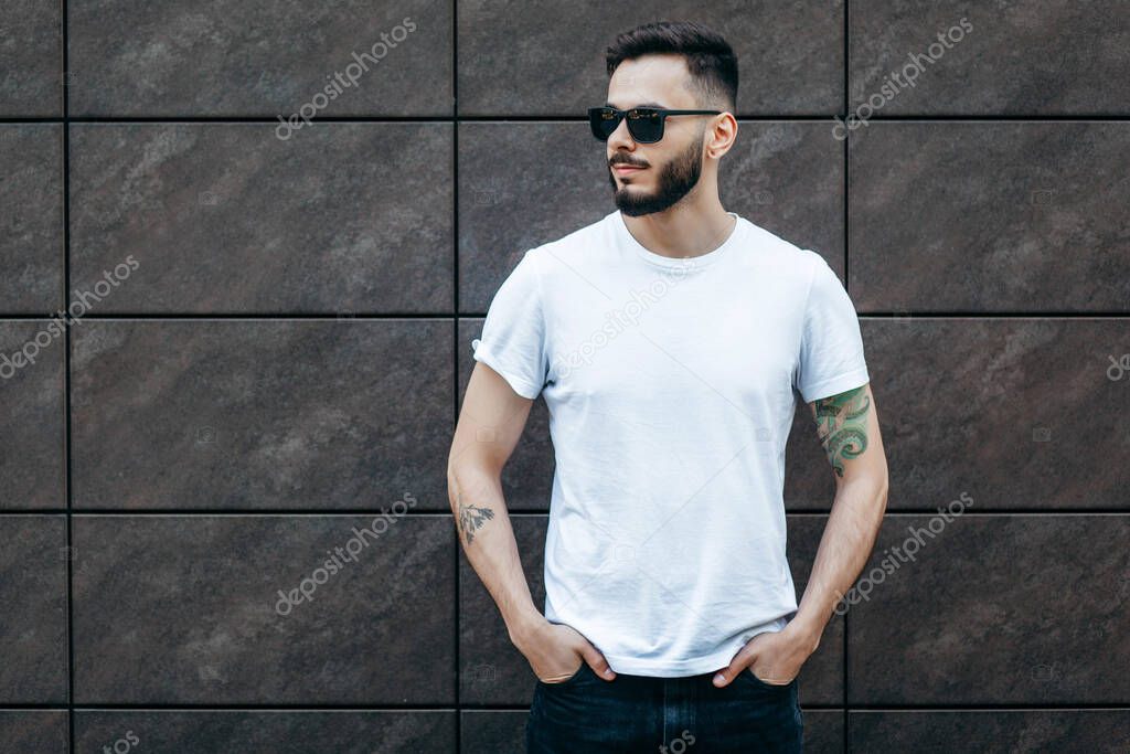A young stylish man with a beard in a white T-shirt and glasses. Street photo