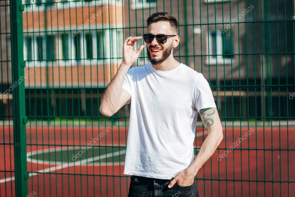 A young stylish man with a beard in a white T-shirt and glasses. Street photo
