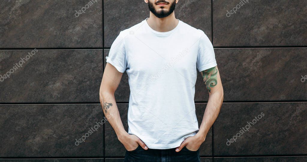 A young stylish man with a beard in a white T-shirt and glasses. Street photo