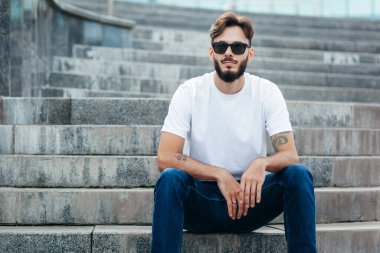 Beyaz tişörtlü ve gözlüklü, sakallı, şık bir genç. Sokak fotoğrafı