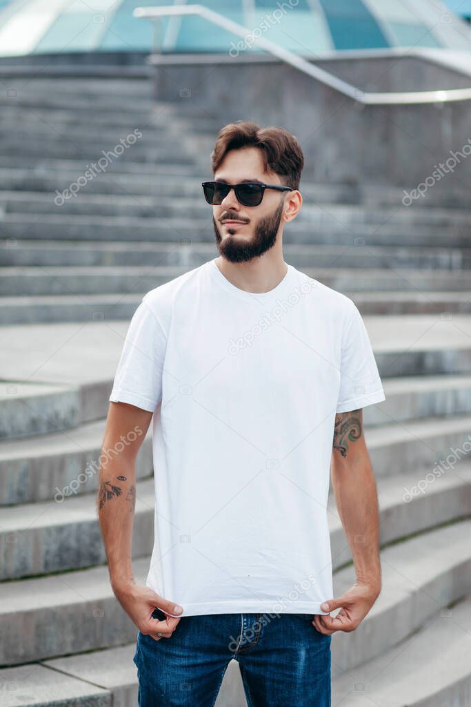 A young stylish man with a beard in a white T-shirt and glasses. Street photo