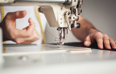 Yakın plan erkek elleri dikiş makinesine kumaş dikiyor.