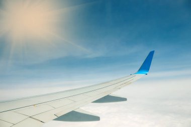 Mavi arka planda bulutların üzerinde uçan bir uçağın kanadı.