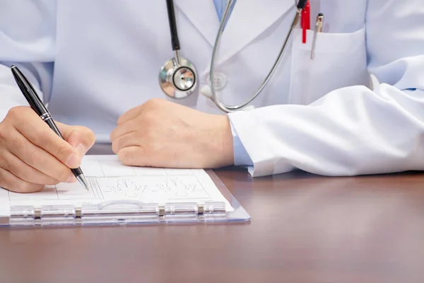 Um médico masculino escrevendo na forma médica com o estetoscópio nas proximidades . — Fotografia de Stock