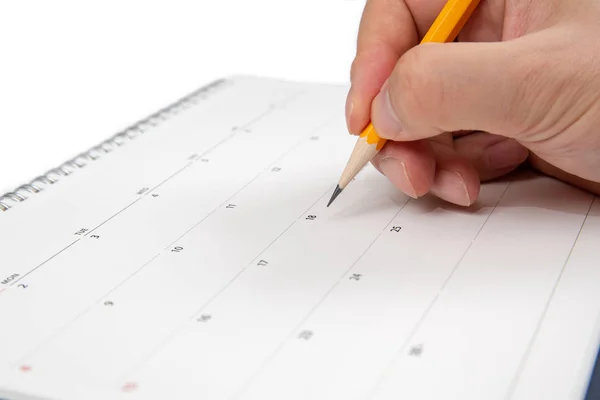 A mans hand holding a pencil in his hand and writing on a calendar. Stock Picture