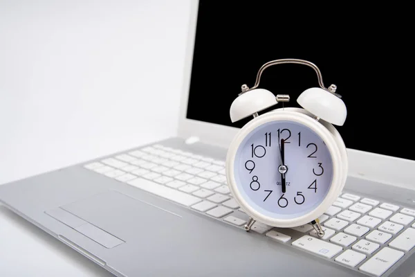 Alarm clock and portable computer put on the desk, with white background.