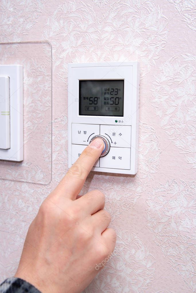 A male hand adjusting the room temperature in winter.