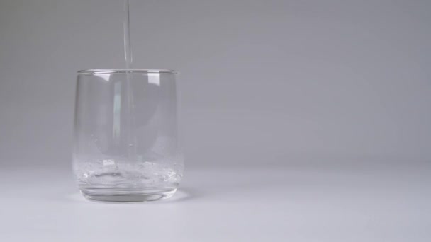 Verser de l'eau dans une tasse en verre sur fond blanc .