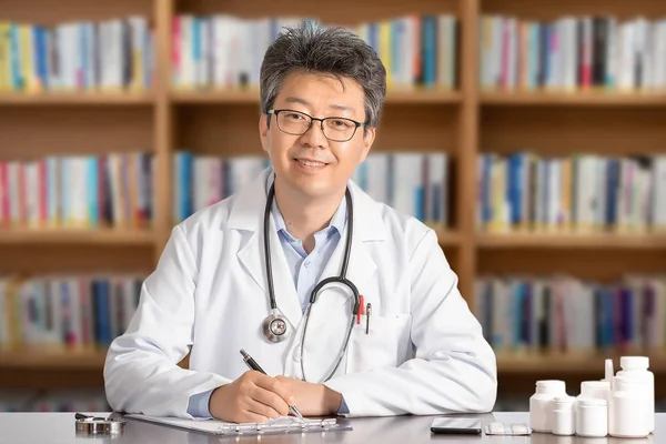 Ásia masculino médico sentado no mesa sorrindo — Fotografia de Stock