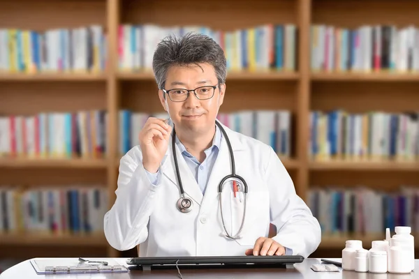 Asyalı erkek doktor masada gülümseyerek oturuyor — Stok fotoğraf