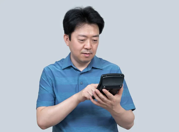 灰色の背景に彼の手に電卓を持っている中年のアジア人男性 — ストック写真
