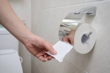 Bir el bej kaplamalı bir banyoda tuvalet kağıdına uzanır..