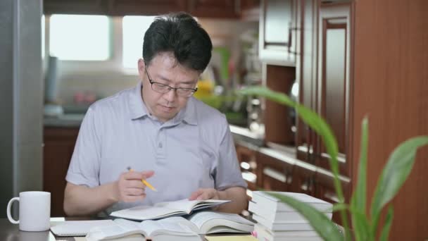 Asiatischer Mann Mittleren Alters Sitzt Hause Schreibtisch Liest Ein Buch — Stockvideo