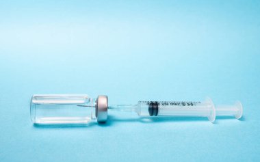 Mavi arka planda şırınga ve ampul ile aşı kavramı.