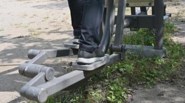 Ağır çekim. Parkta yürüyen bir makineyle çalışan orta yaşlı bir adamın ayaklarına yakın plan..