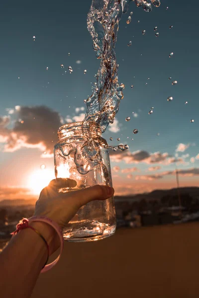 In the image can see water explosion and a beautiful sunset in background.