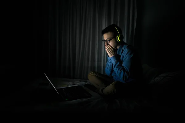 Man watching tv in a laptop sitting on a bed in the night at home