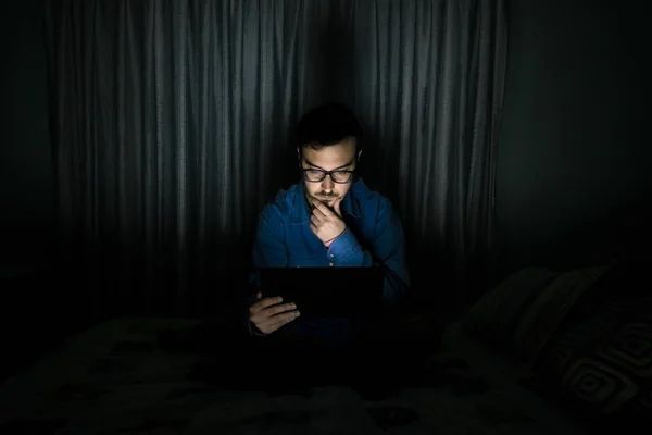 Man watching tv series in a tablet sitting on a bed in the night at home