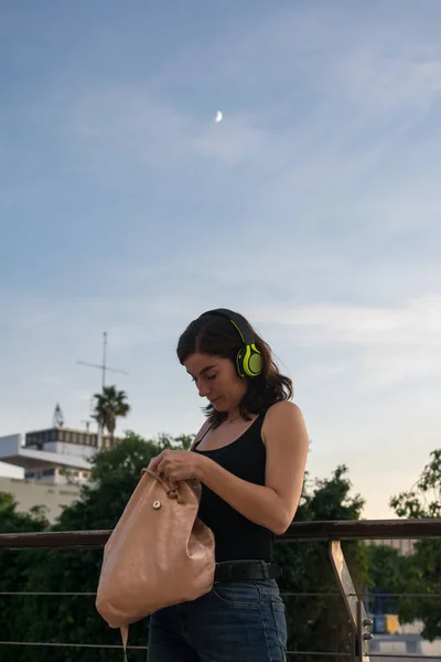 Young woman is searching something in her bag while she is listening music