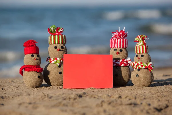 Familie van zand sneeuwpoppen op tropisch strand met blanco kaart. — Stockfoto